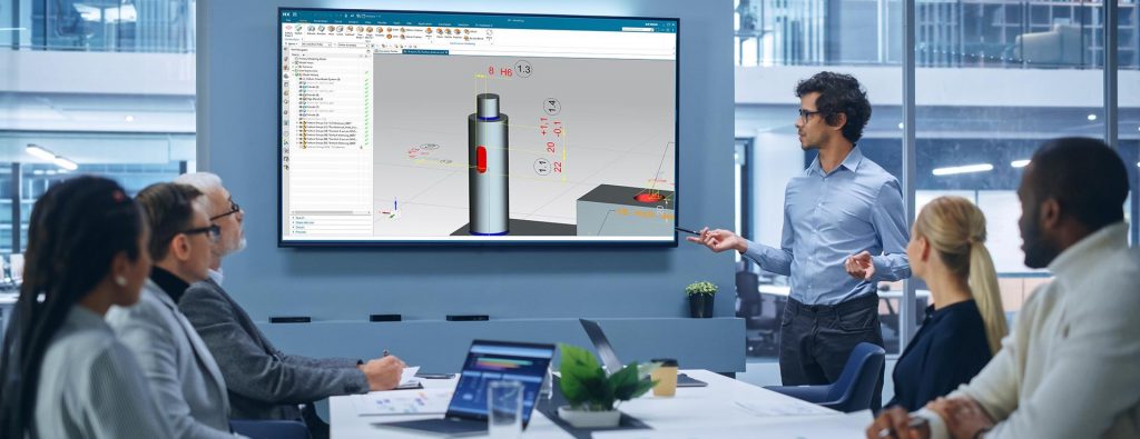 Fuerungskraft steht vor Team und zeigt auf Monitor mit 3D Modell mit PMI in Siemens NX