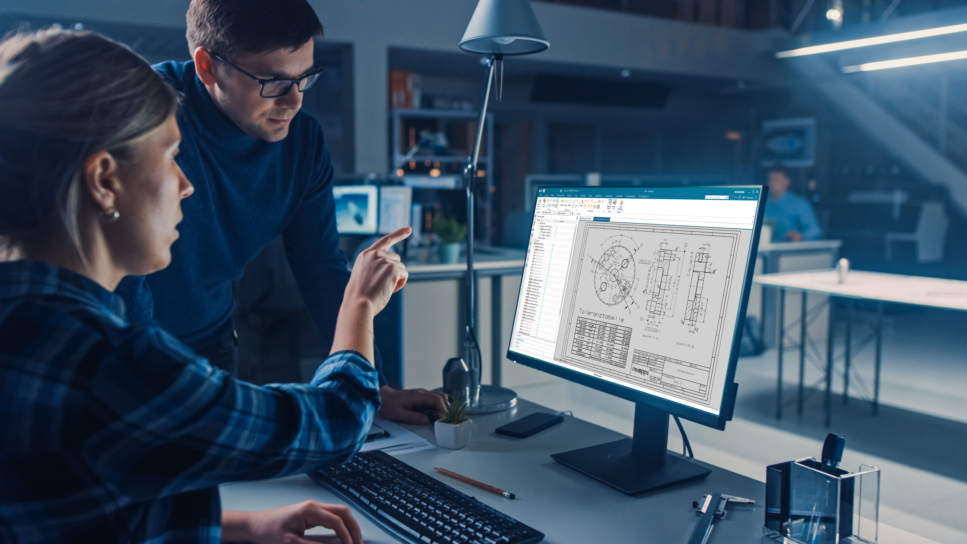 Zwei Personen zeigen auf Bildschirm mit Siemens NX Toleranztabelle